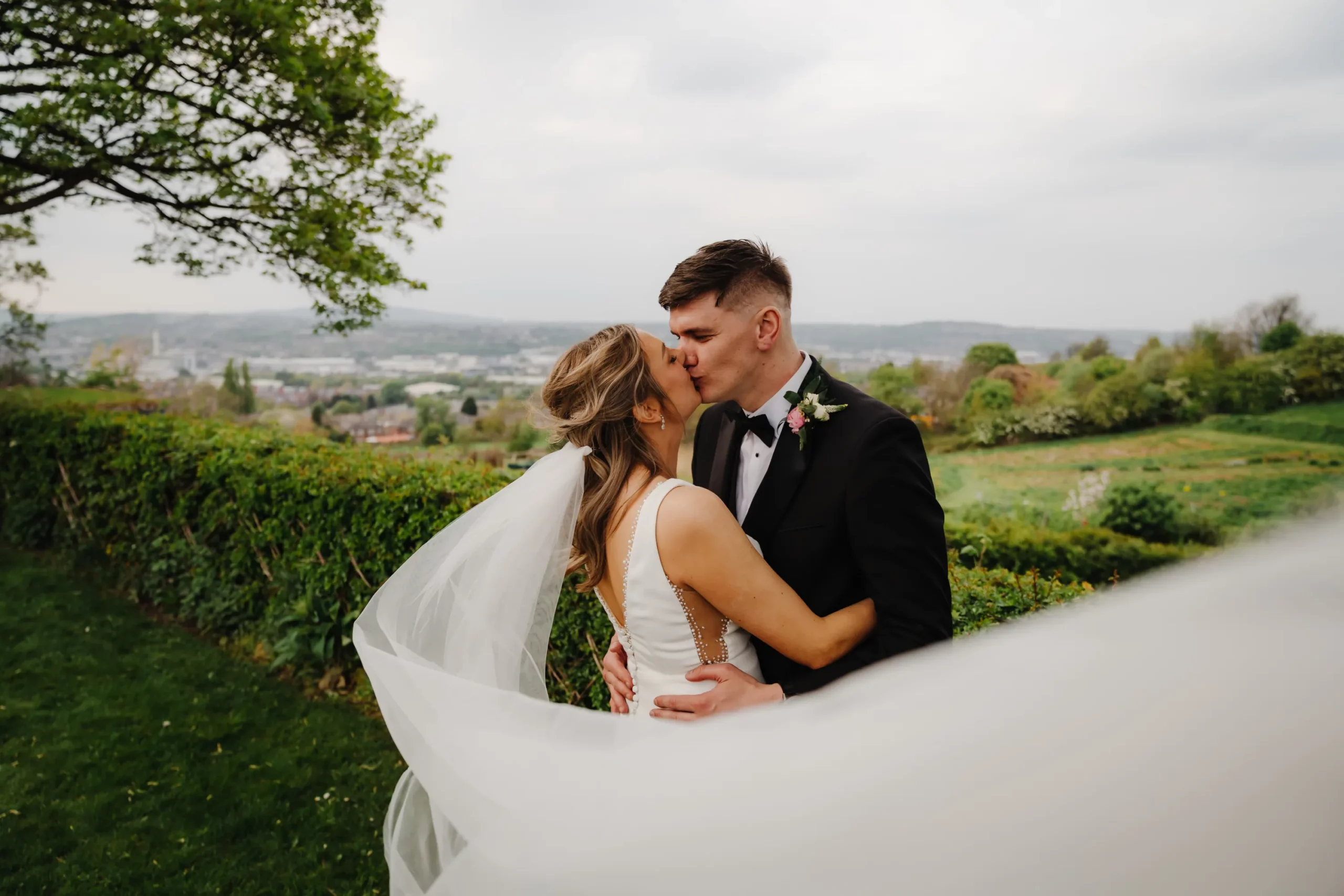 A man and woman snogging in front of bushes. Bethany Maeve Photography