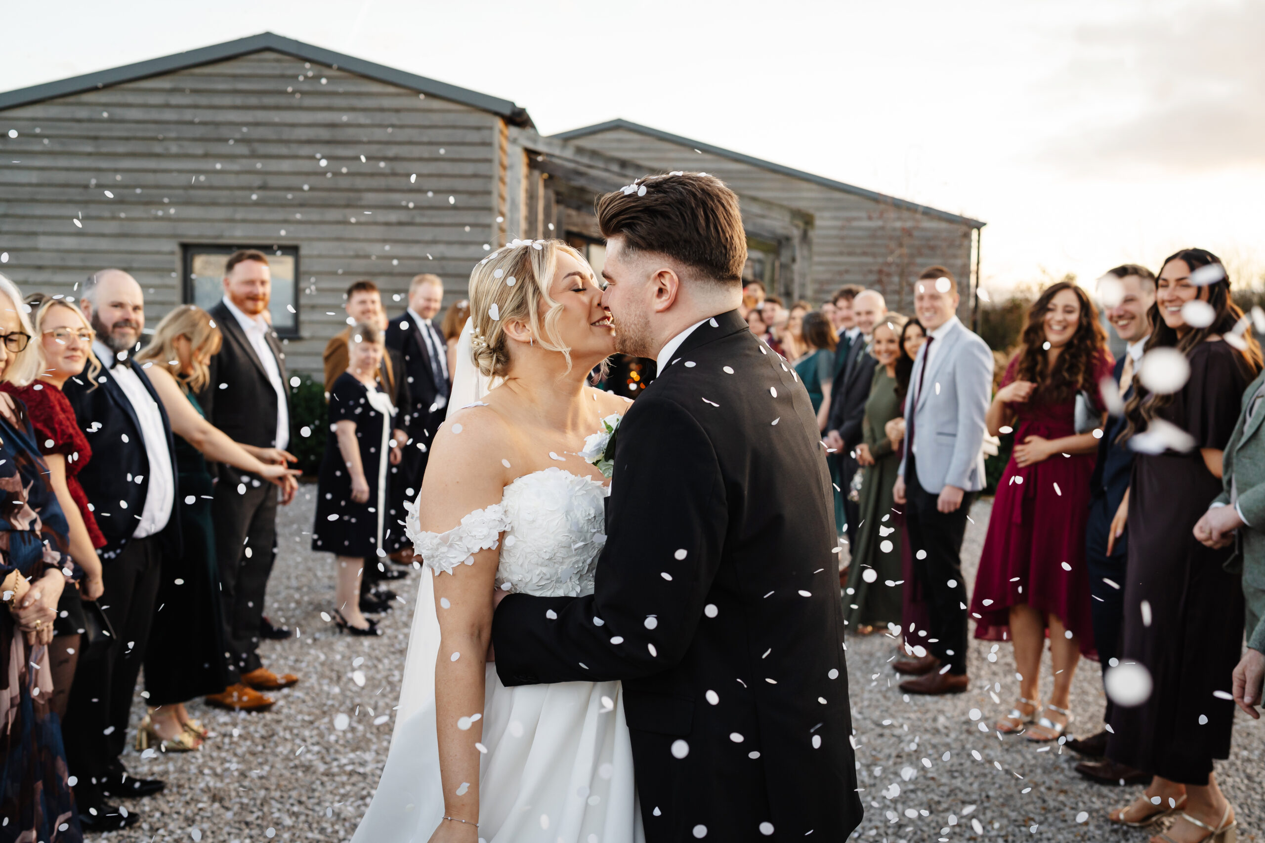 Bride and groom kissing amid wedding guests confetti at Stretton Manor Barn for a black tie wedding