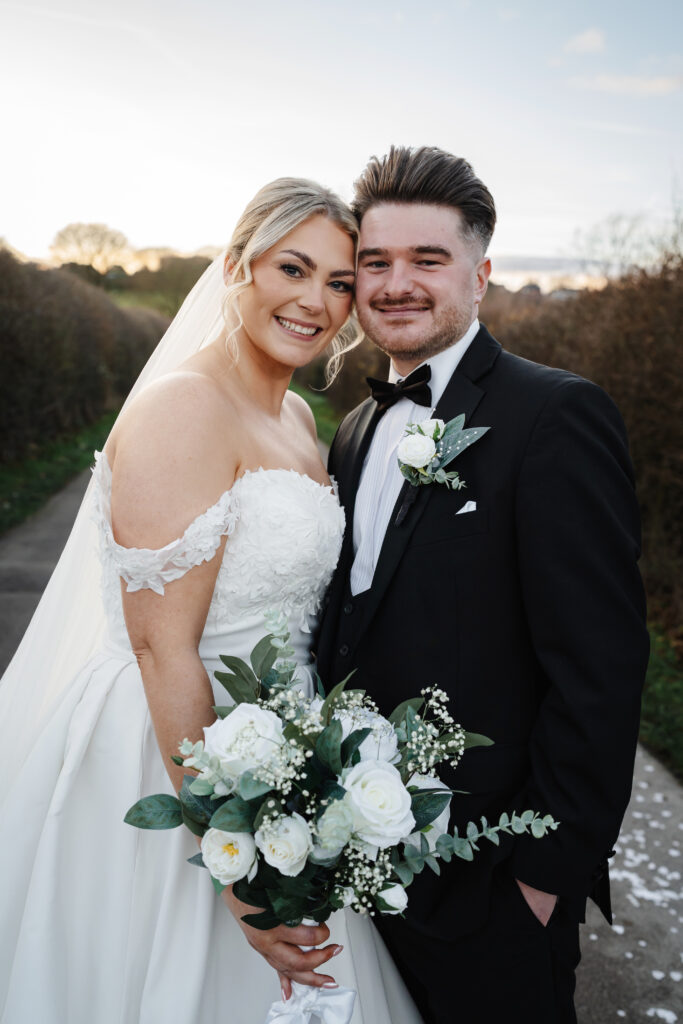 Newlywed couple posing with white rose bouquet
