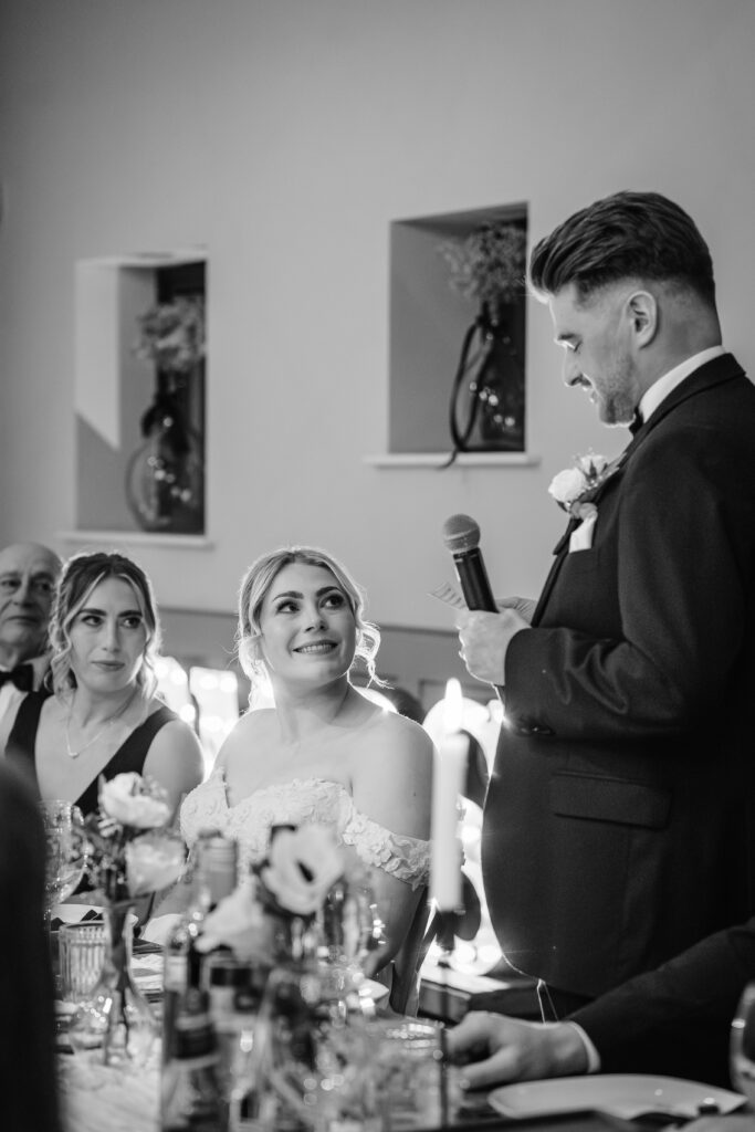 Groom giving speech to smiling bride at wedding reception