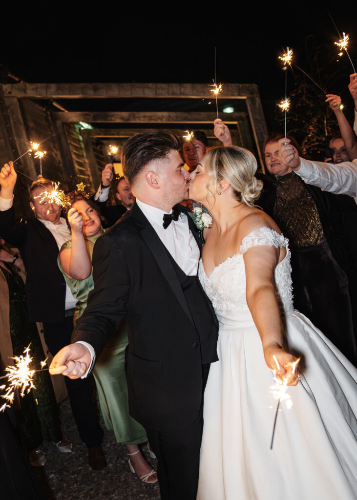 Newlyweds kissing surrounded by sparklers at night